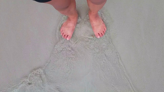 声音包括在内。在沙滩上赤裸的脚顶视图。泡沫海纹理背景海洋，同时赤脚站在沙滩上细沙。在沙子和海泡沫腿的观点。夏天的概念。视频素材