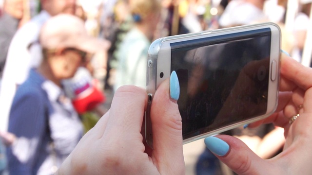 女孩的手在智能手机上取下的特写，一大群人走在街上视频素材