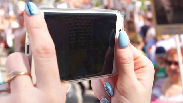 女孩的手在智能手机上取下的特写一大群人走在街上，慢镜头视频素材