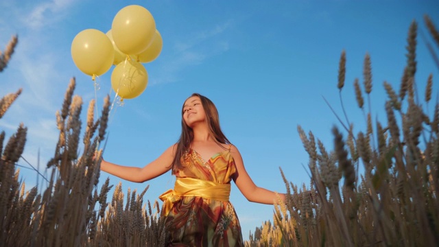 一个年轻的女孩带着黄色的气球走在麦田里视频下载