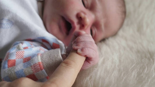 婴儿新生儿抱紧大人的手指，母亲父亲的手捏住婴儿视频素材