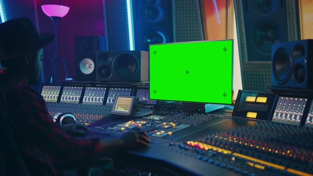 时尚的音频工程师/制作人工作在音乐唱片工作室，使用绿色屏幕色度键计算机显示，混音板均衡器和控制台创建新的热门歌曲。黑人艺术家音乐家视频下载