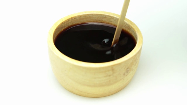 木杯里的黑咖啡和白色背景上的木头做的咖啡球拍。缓慢的运动。视频下载