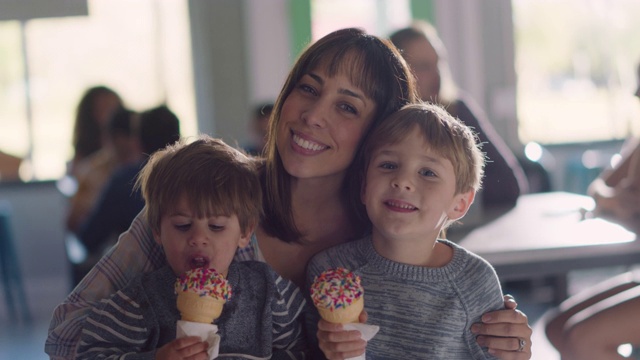 一个母亲和她的两个儿子一起吃冰淇淋，亲吻她的脸颊视频素材