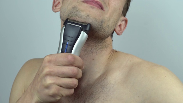 一个非常多毛的男人理发的特写，他的身体毛发，男性胸部自己用一个剪子，电动剃须刀，三聚体。孤立在白色背景上。裸男刮他的胸毛视频下载