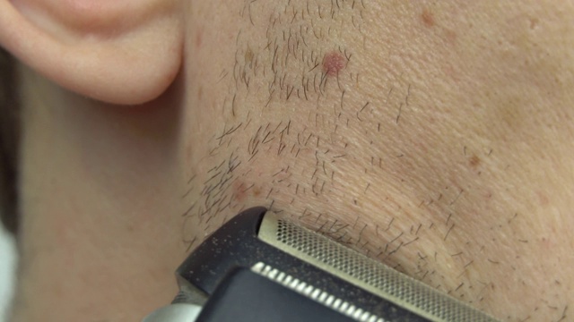 年轻人用电动剃须刀刮胡子。这家伙用剃须刀剃胡子。视频下载
