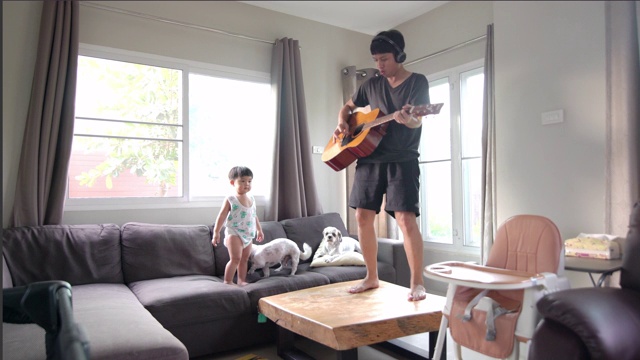 快乐的父亲和儿子还有两只狗在客厅玩吉他。视频下载