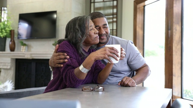 一个成熟的男人在退休中心边喝咖啡边聊天边拥抱和亲吻他年迈的母亲视频素材