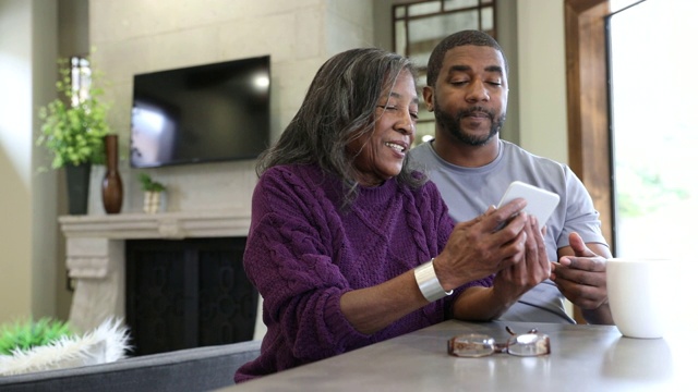 一名男子用智能手机在家协助他年迈的母亲进行远程医疗视频会议视频素材