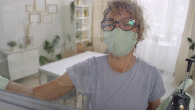 戴面罩的妇女在玻璃上喷洒消毒剂视频素材