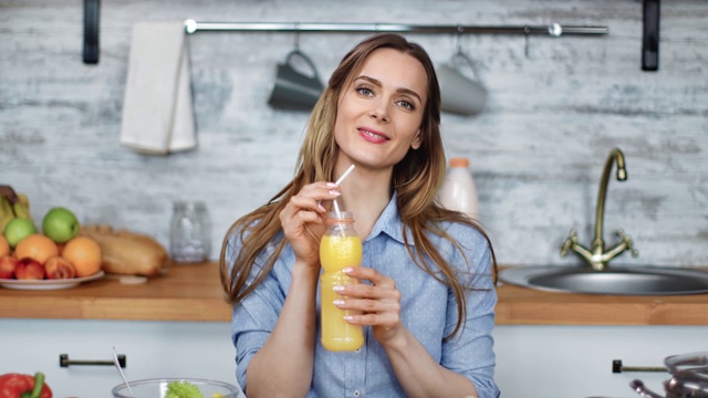 微笑的年轻金发女人喝新鲜橙汁的肖像。红色摄像机中拍摄视频素材