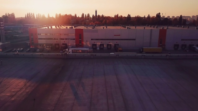 在美丽的夕阳下，飞过物流中心仓库的屋顶，飞过装载货物的卡车视频下载