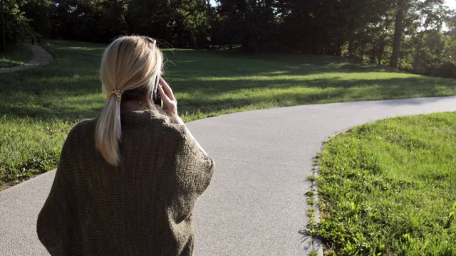 成熟的健康女人在春天的一天在公园里使用电话和交谈视频下载