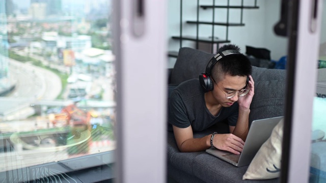 一个亚洲的中国少年男孩在家学习，在客厅用笔记本电脑视频素材