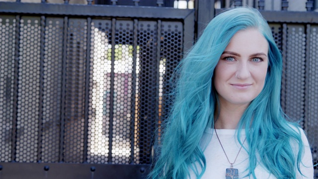一个美丽独特的活力时尚的年轻女人与有趣可爱的蓝绿色头发染色站在户外在夏天摆姿势的慢镜头视频素材