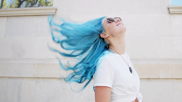 抛头发的一个独特的，活泼的，时尚的，快乐的，快乐的年轻女人与有趣可爱的蓝绿色染头发站在户外在夏天视频下载