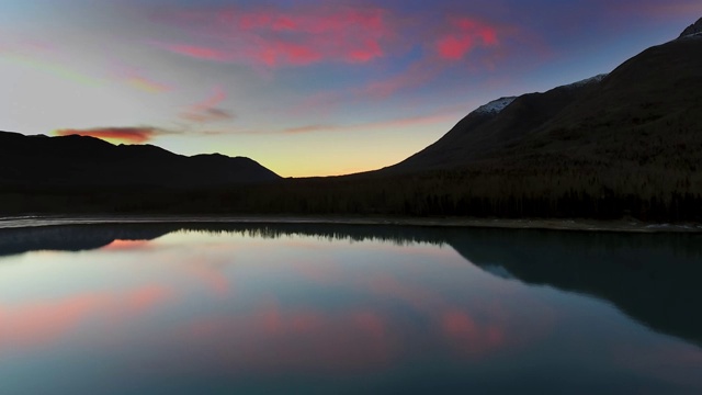空中拍摄的黑暗山脉与茂密的森林和粉红色的日落在一个清澈的湖(埃克鲁特纳湖，阿拉斯加，美国)视频素材