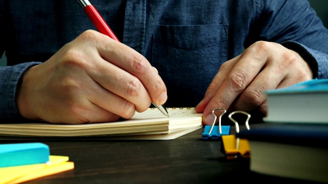 一个男人在桌子上的笔记本上写字。特写的手与一支笔。视频素材