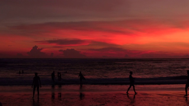 日落海滩的风景与年轻的冲浪者与冲浪板和人们在假期沿着巴厘岛海岸散步视频素材