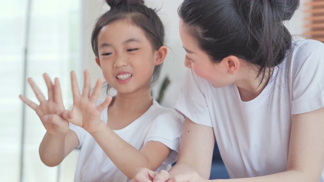 快乐的亚洲女儿，6-7岁的孩子数数用手指和母亲学习数学。年轻的父母母亲教学校的孩子女孩帮助家庭作业学习坐在家里的桌子上。儿童教育理念、家庭教育和远程教育视频下载