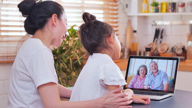 亚洲母亲和女儿在视频会议上与国外的祖父母家庭视频电话，在社会距离使用笔记本电脑和视频会议技术。社会电话会议视频下载