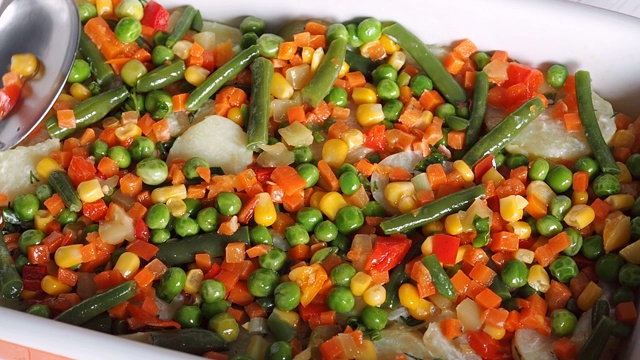 在烤盘里撒上煮熟的土豆和青豆、玉米、豌豆、胡椒的混合蔬菜。墨西哥砂锅土豆配蔬菜。视频下载