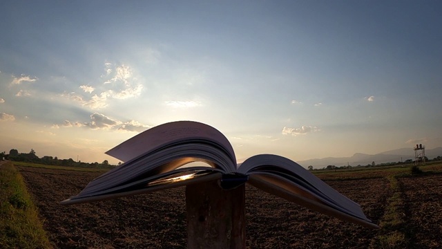 书页被风轻轻吹在田野上的夕阳天空背景上。暑假生活方式与教育理念。视频素材