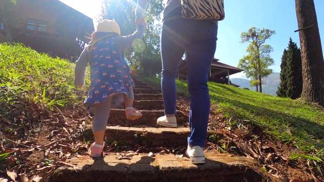 夏日里，小女孩牵着妈妈的手走在公园的楼梯上。幸福的家庭时间。视频素材