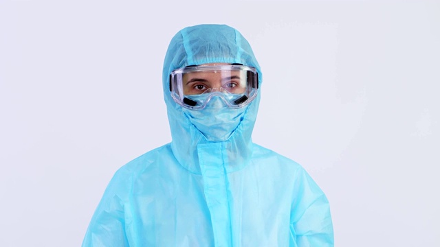 女医生或护士，穿着特殊防护服、制服、面罩、眼镜，看着摄像机，手心、手心显示停止标志。冠状病毒流行。白色背景。冠状病毒保护视频下载