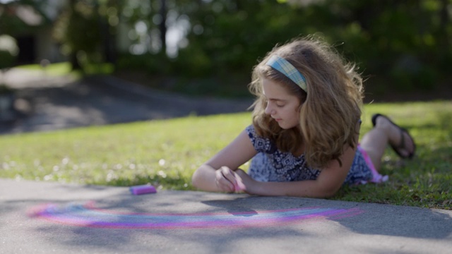 精神集中的女孩专注于在她的车道上画粉笔彩虹视频素材