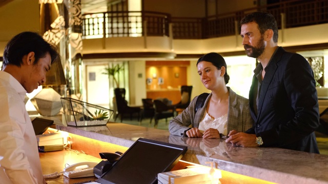 在酒店办理入住手续的商业伙伴或同事。年轻夫妇和接待员在酒店柜台视频素材