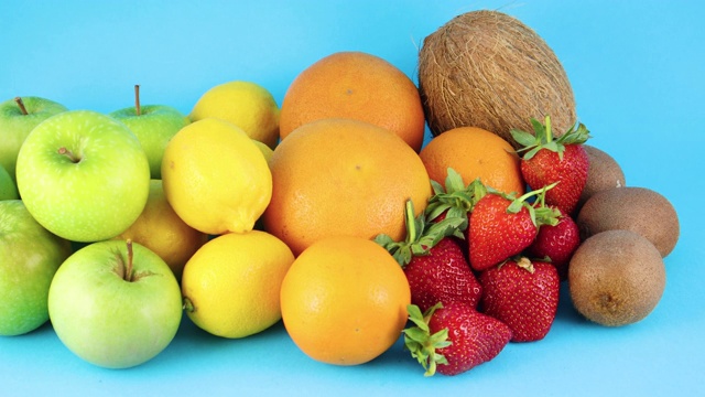 蓝色背景上的不同新鲜有机水果堆。橘子，苹果，猕猴桃，草莓，柠檬和椰子视频下载