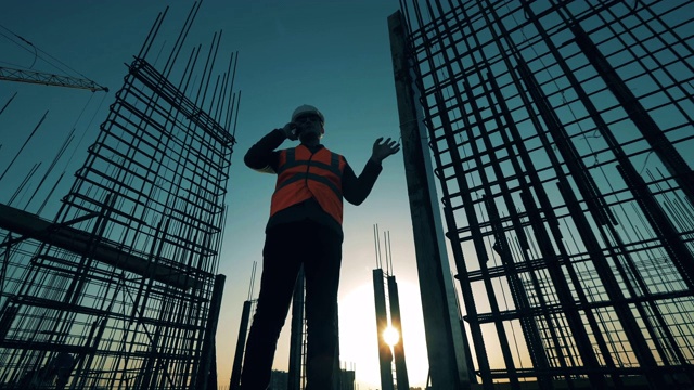 一名男性工程师站在日落背景的工地上打电话。视频素材