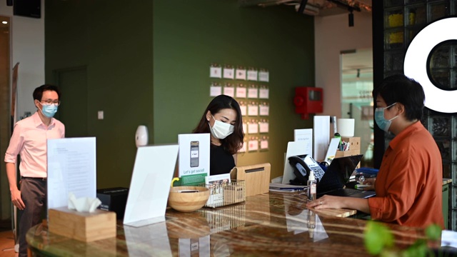 一名亚洲华人接待员正在执行预防疾病的标准操作程序，测量访客、同事和同事的体温，并记录他们的个人数据视频下载