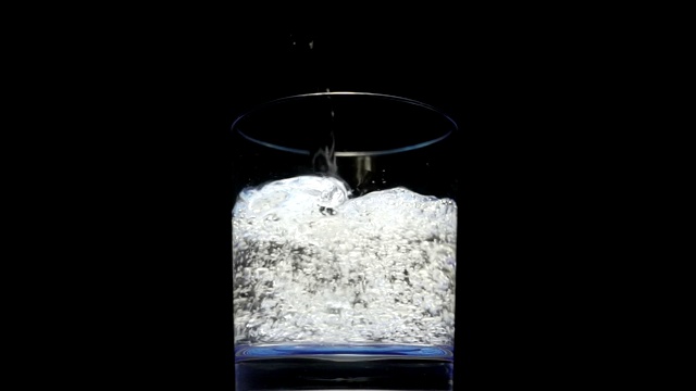 将苏打水从瓶子中倒入一个以黑色为背景的玻璃杯中视频素材