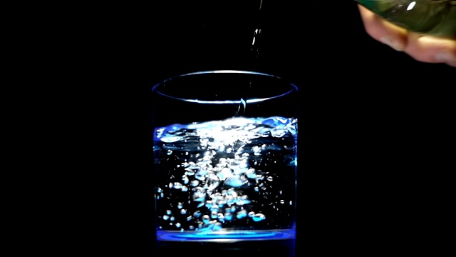 将清澈的水从瓶子中倒入一个黑色背景的玻璃杯中视频素材