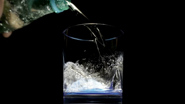 将苏打水从瓶子中倒入一个以黑色为背景的玻璃杯中视频素材