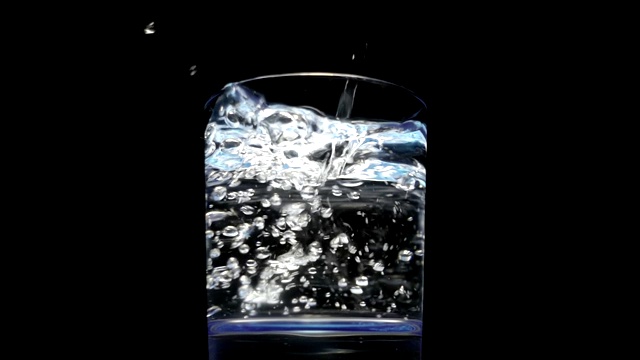 将清澈的水从瓶子中倒入一个黑色背景的玻璃杯中视频素材