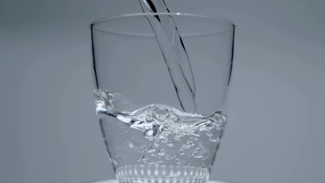 从瓶子中倒入晶莹剔透的水到一个白色背景的玻璃杯中视频素材