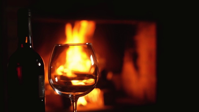 壁炉前的桌上放着一瓶红葡萄酒，迎着火焰。视频下载