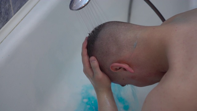 一个长着蓝色头发的年轻人在洗头。一个男人洗掉头发上的蓝色颜料。视频素材