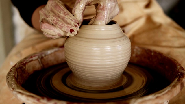 女陶工的手，红色的指甲，工作与湿粘土在一个陶器轮制作粘土产品在车间。一个面目全非的女人做了一个花瓶，把它拉了起来视频下载