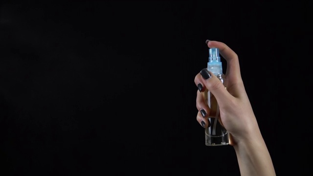 女人在黑色背景上洒香水。手里拿着一瓶香水特写。慢动作视频素材
