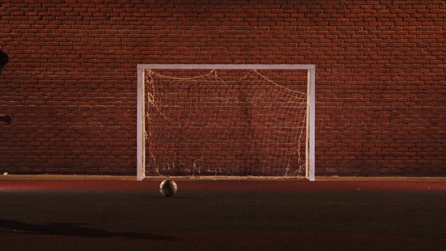 一个年轻人晚上在操场上踢足球，在大门里踢球视频下载