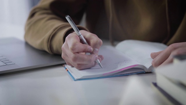 千禧年白人男孩的手在练习册上写字。特写的男性手掌与笔。勤奋的大学生做作业。教育，学习，学习，生活方式。视频素材