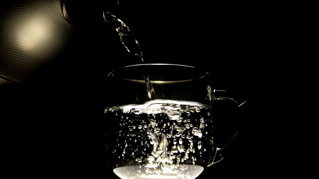 将开水从闪亮的金属茶壶中倒入玻璃杯中视频素材