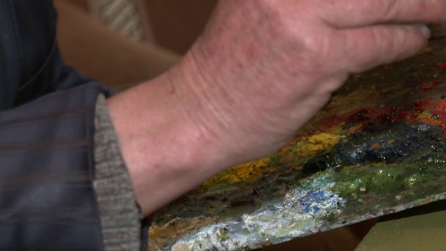 一位老艺术家用画笔和一个特写调色板蘸着油彩作画。画家用画笔在色彩鲜艳的调色板上作画的手视频下载