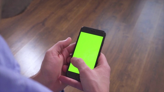 男人的手拿着智能手机并使用它。设备上的绿色屏幕。在电子键盘上打字，并向右、上、下滑动。视频下载