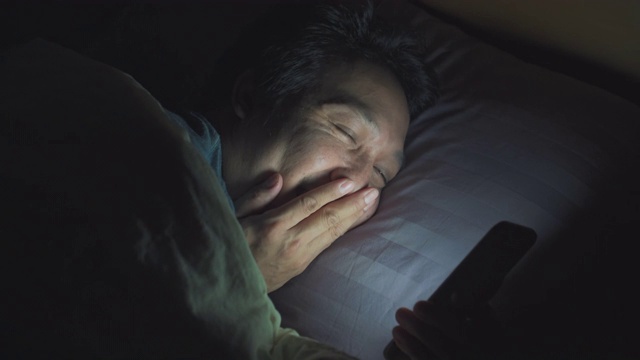 亚洲男人晚上在床上玩智能手机视频素材