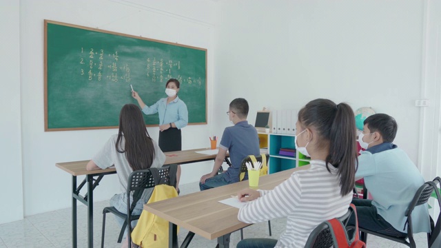 一群亚洲小学生和教师戴着卫生口罩在教室里防止Covid - 19的爆发，返校时重新开学，教育理念的新常态。视频下载